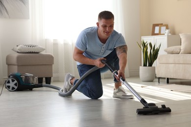 Photo of Man cleaning floor with vacuum cleaner at home