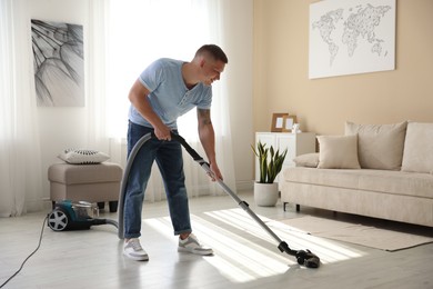 Photo of Man cleaning floor with vacuum cleaner at home