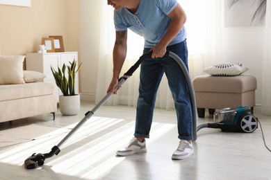 Photo of Man cleaning floor with vacuum cleaner at home, closeup