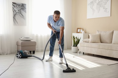 Photo of Man cleaning floor with vacuum cleaner at home