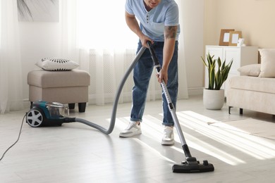 Photo of Man cleaning floor with vacuum cleaner at home, closeup
