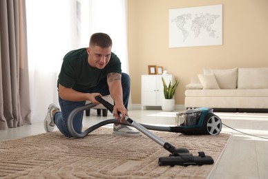 Photo of Man cleaning carpet with vacuum cleaner at home
