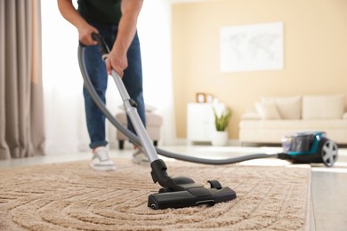 Photo of Man cleaning carpet with vacuum cleaner at home, closeup