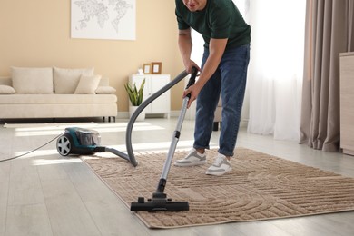 Photo of Man cleaning carpet with vacuum cleaner at home, closeup