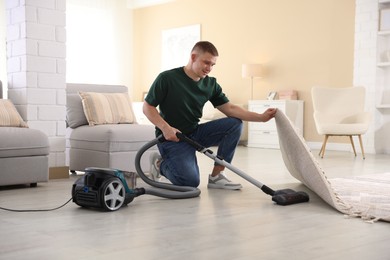 Photo of Man cleaning floor with vacuum cleaner at home