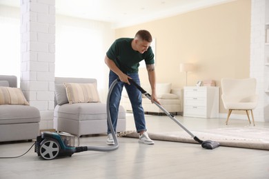 Photo of Man cleaning floor with vacuum cleaner at home