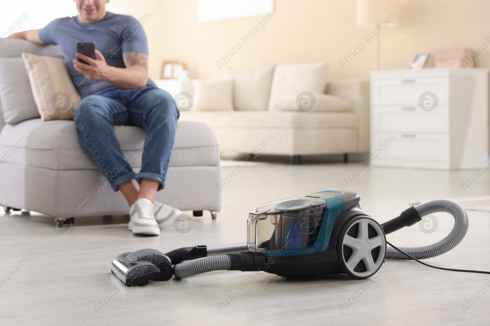 Man with smartphone on sofa at home, focus on vacuum cleaner Photo of Man with smartphone on sofa at home, focus on vacuum cleaner