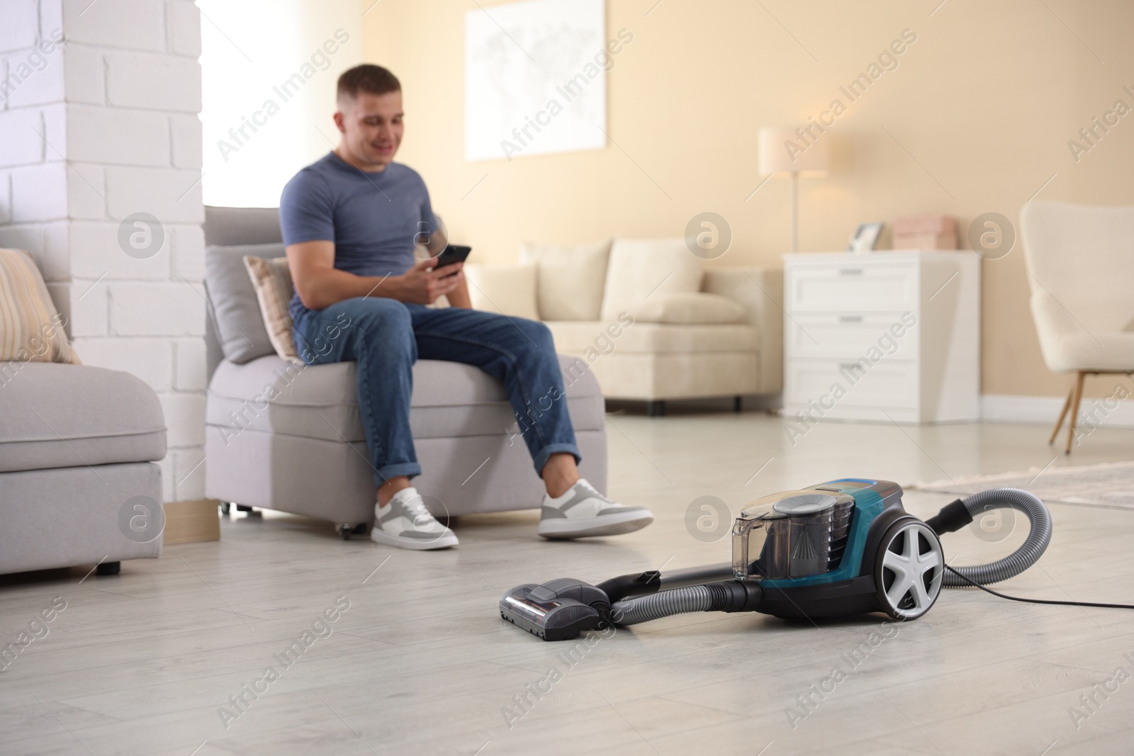 Man with smartphone on sofa at home, focus on vacuum cleaner Photo of Man with smartphone on sofa at home, focus on vacuum cleaner
