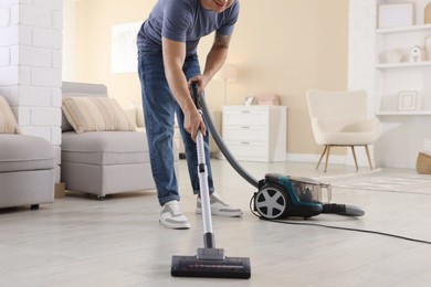 Photo of Man cleaning floor with vacuum cleaner at home, closeup