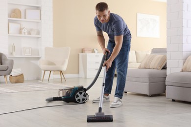 Photo of Man cleaning floor with vacuum cleaner at home