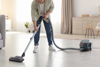 Photo of Man cleaning floor with vacuum cleaner at home, closeup
