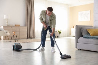 Photo of Man cleaning floor with vacuum cleaner at home