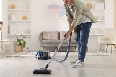 Photo of Man cleaning floor with vacuum cleaner at home, closeup