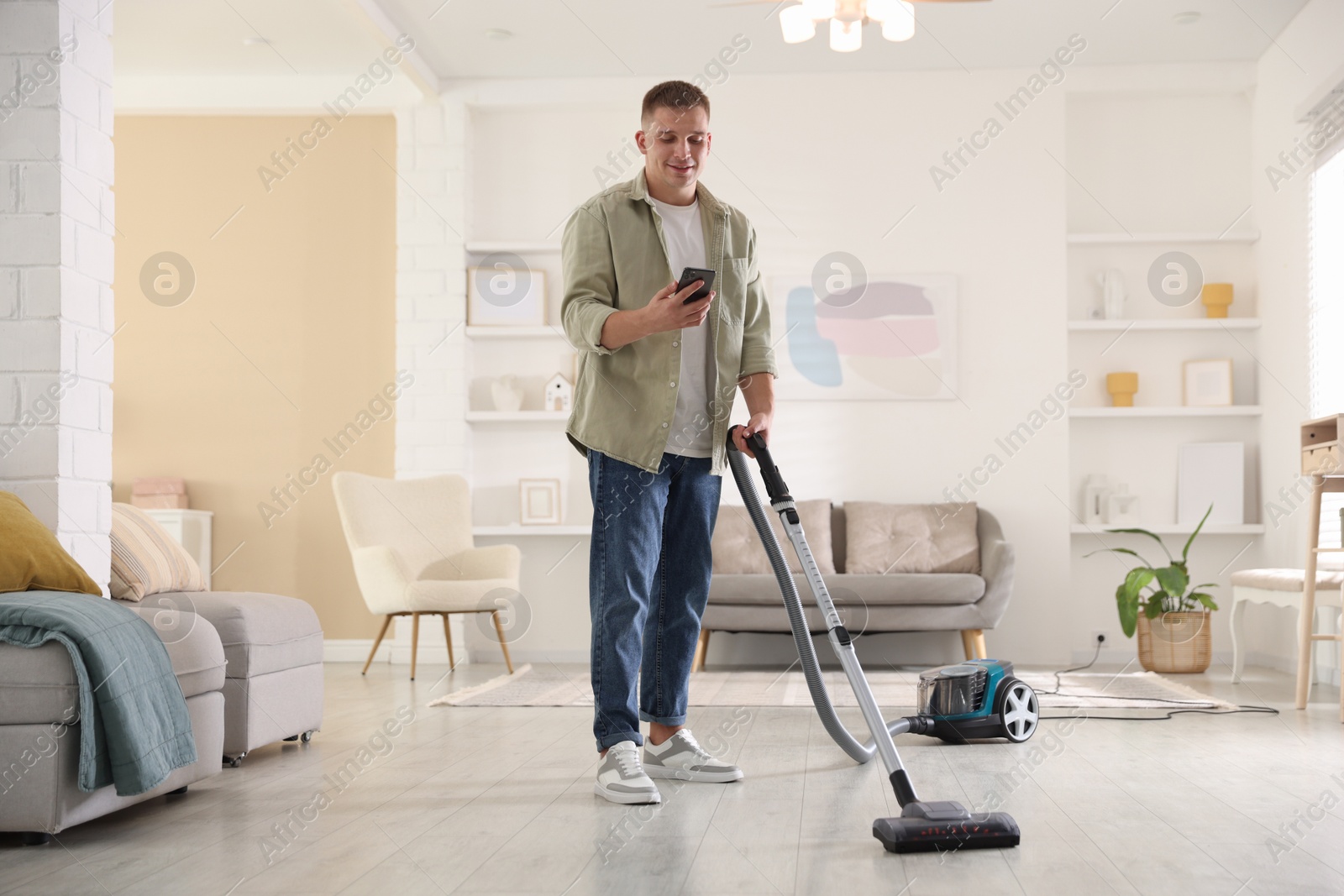 Man with smartphone cleaning floor with vacuum cleaner at home Photo of Man with smartphone cleaning floor with vacuum cleaner at home
