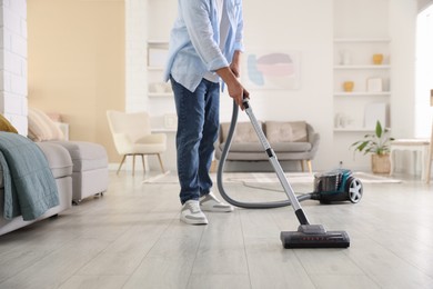 Photo of Man cleaning floor with vacuum cleaner at home, closeup