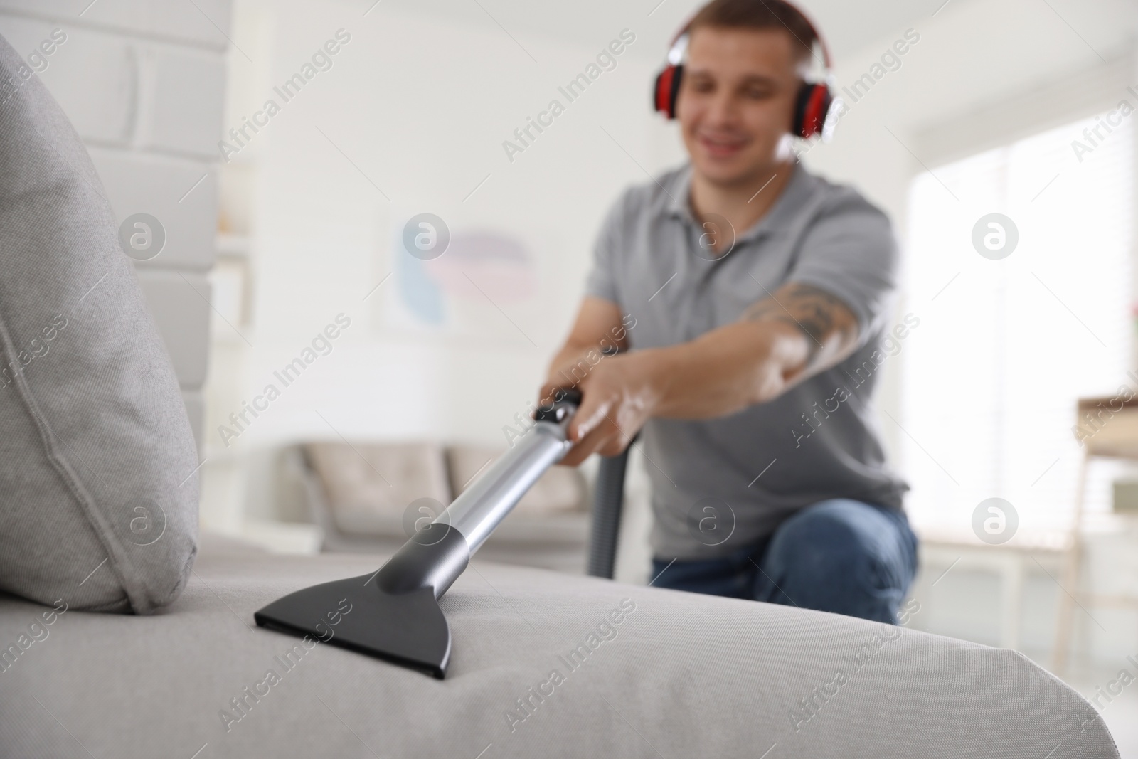 Man in headphones cleaning sofa with vacuum cleaner at home, selective focus Photo of Man in headphones cleaning sofa with vacuum cleaner at home, selective focus