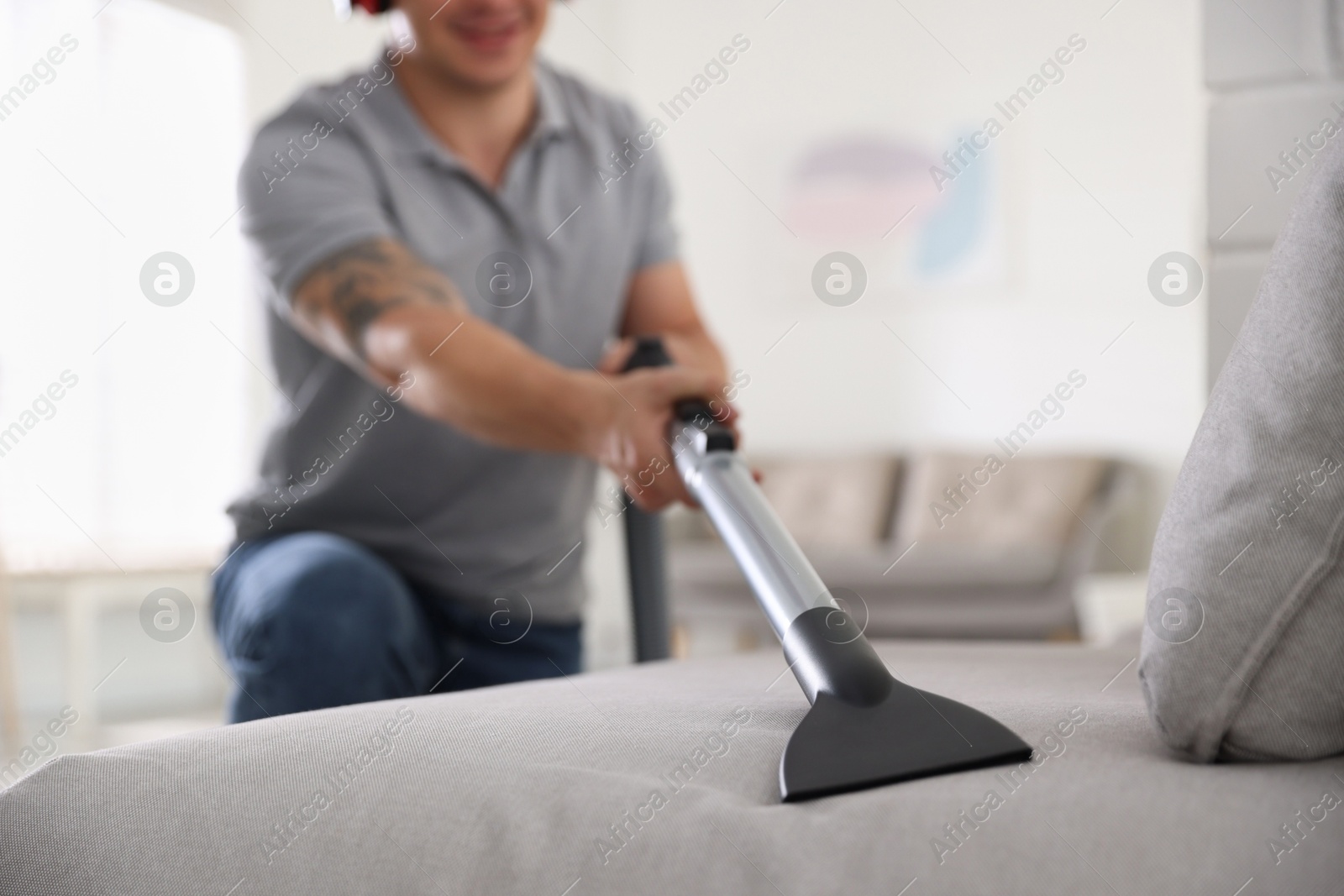 Man cleaning sofa with vacuum cleaner at home, closeup Photo of Man cleaning sofa with vacuum cleaner at home, closeup