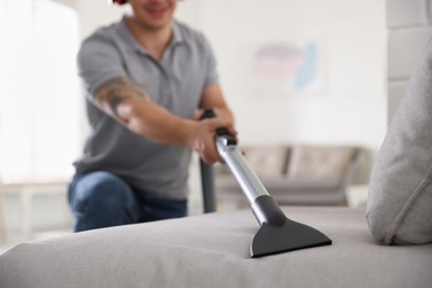 Photo of Man cleaning sofa with vacuum cleaner at home, closeup