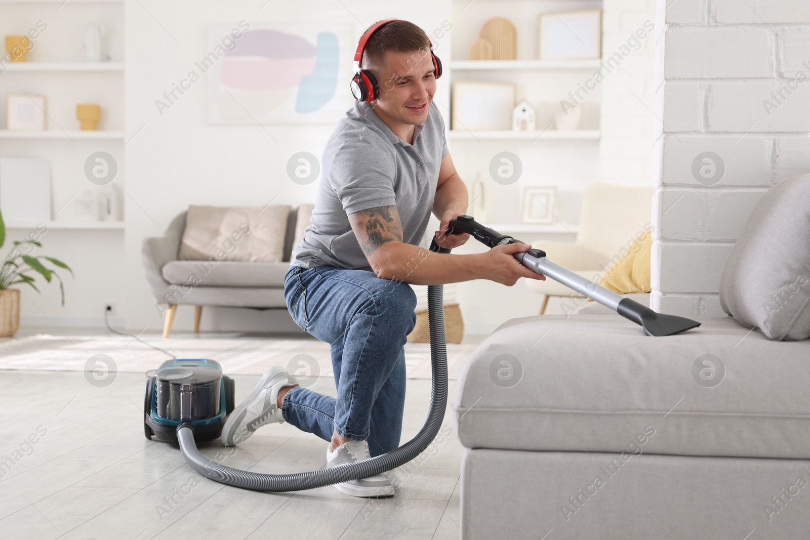 Man in headphones cleaning sofa with vacuum cleaner at home Photo of Man in headphones cleaning sofa with vacuum cleaner at home