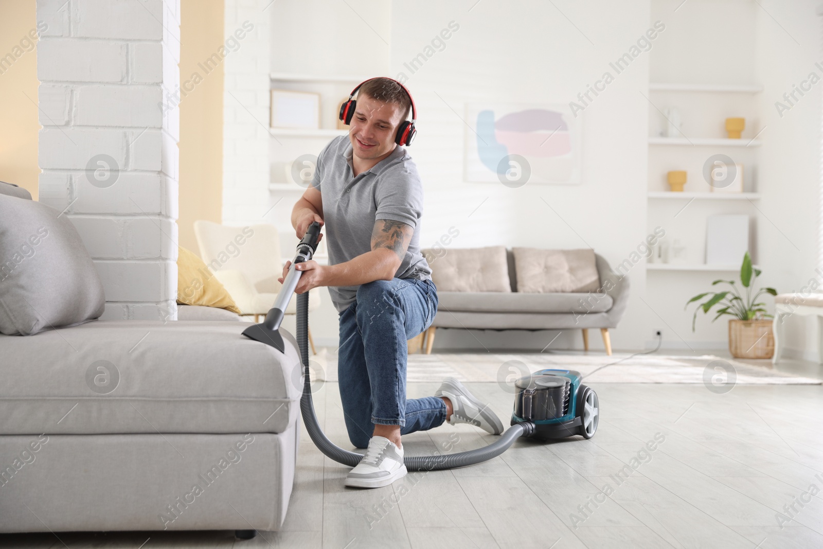 Man in headphones cleaning sofa with vacuum cleaner at home Photo of Man in headphones cleaning sofa with vacuum cleaner at home