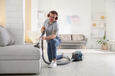 Photo of Man in headphones cleaning sofa with vacuum cleaner at home