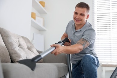 Photo of Man cleaning sofa with vacuum cleaner at home