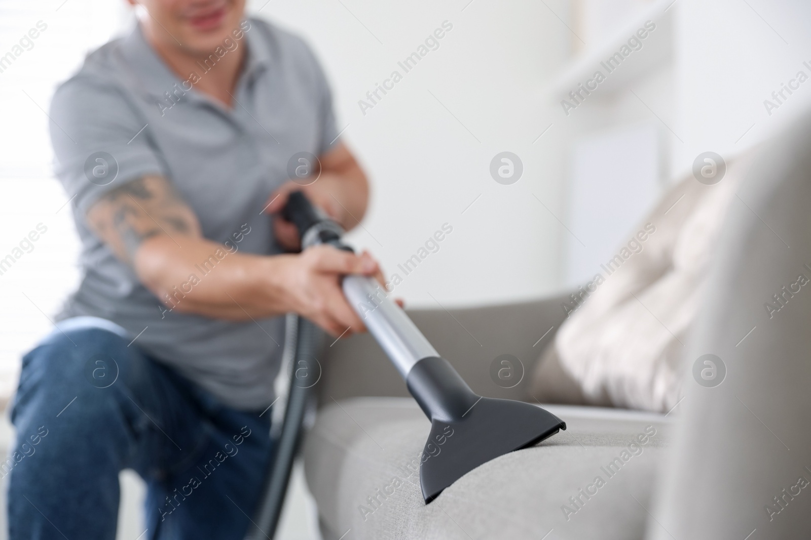 Man cleaning sofa with vacuum cleaner at home, closeup Photo of Man cleaning sofa with vacuum cleaner at home, closeup