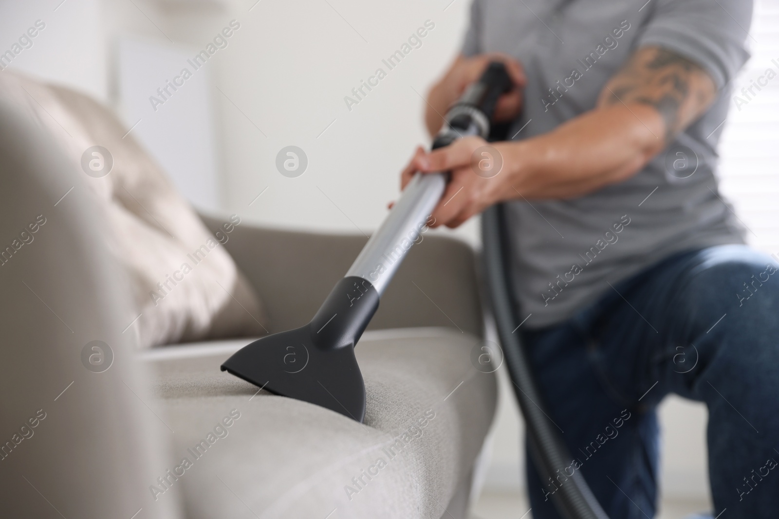 Man cleaning sofa with vacuum cleaner at home, closeup Photo of Man cleaning sofa with vacuum cleaner at home, closeup