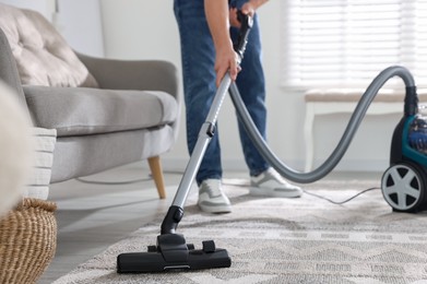Photo of Man cleaning carpet with vacuum cleaner at home, closeup