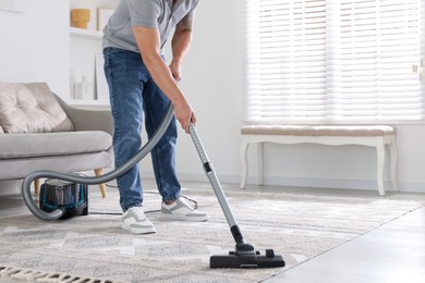 Photo of Man cleaning carpet with vacuum cleaner at home, closeup