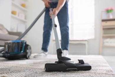 Photo of Man cleaning carpet with vacuum cleaner at home, closeup