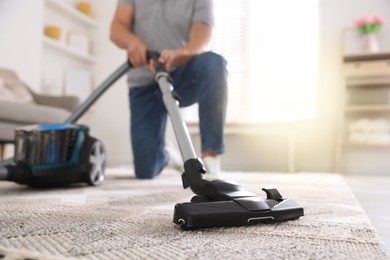 Photo of Man cleaning carpet with vacuum cleaner at home, closeup