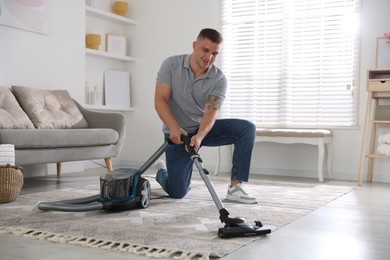 Photo of Man cleaning carpet with vacuum cleaner at home