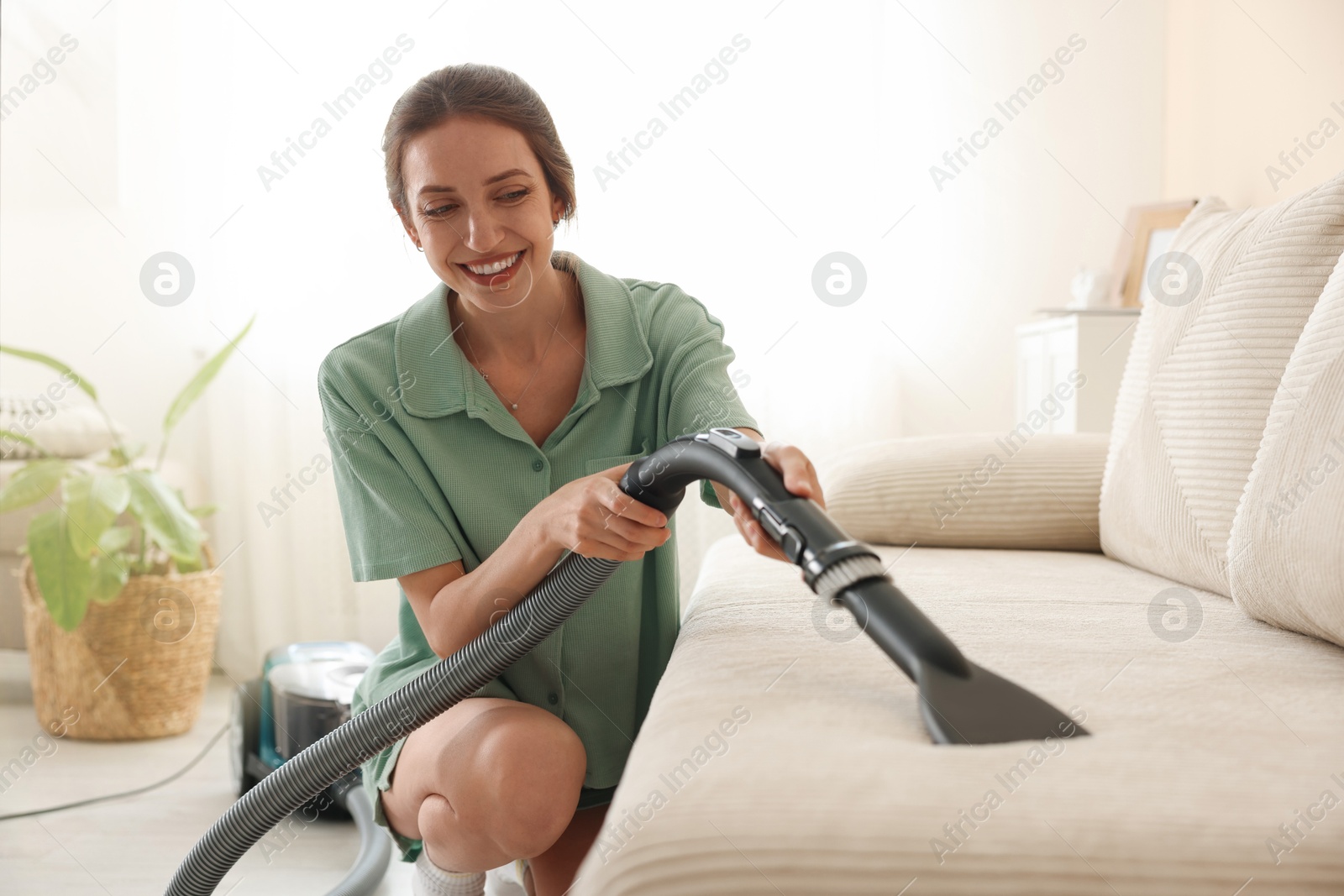 Woman cleaning sofa with vacuum cleaner at home Photo of Woman cleaning sofa with vacuum cleaner at home