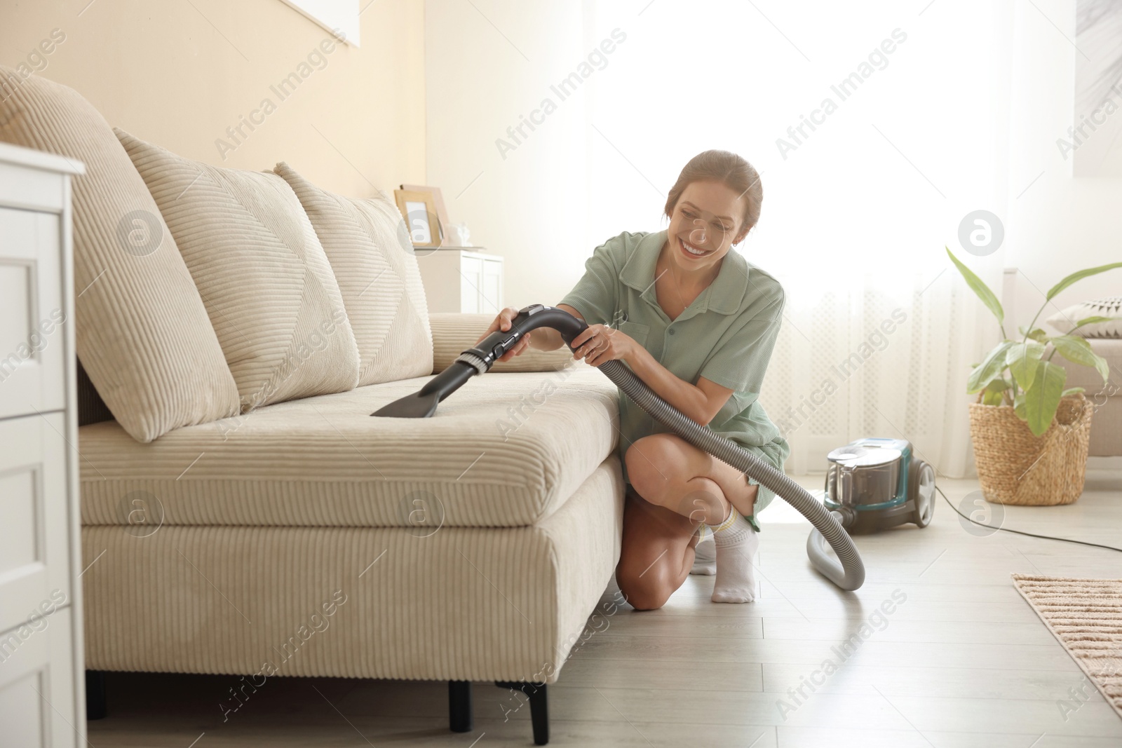 Woman cleaning sofa with vacuum cleaner at home Photo of Woman cleaning sofa with vacuum cleaner at home