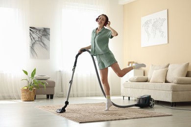 Photo of Woman in headphones cleaning carpet with vacuum cleaner at home