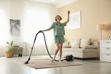 Photo of Woman in headphones cleaning carpet with vacuum cleaner at home