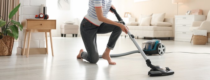 Photo of Woman cleaning floor with vacuum cleaner at home, closeup
