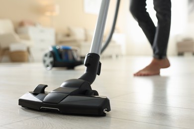 Photo of Woman cleaning floor with vacuum cleaner at home, closeup