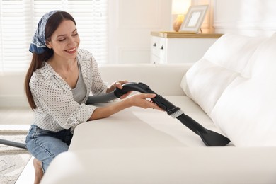 Photo of Woman cleaning sofa with vacuum cleaner at home