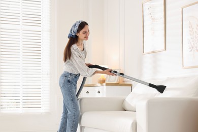 Photo of Woman cleaning sofa with vacuum cleaner at home