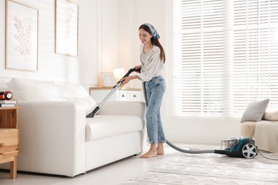 Photo of Woman cleaning sofa with vacuum cleaner at home