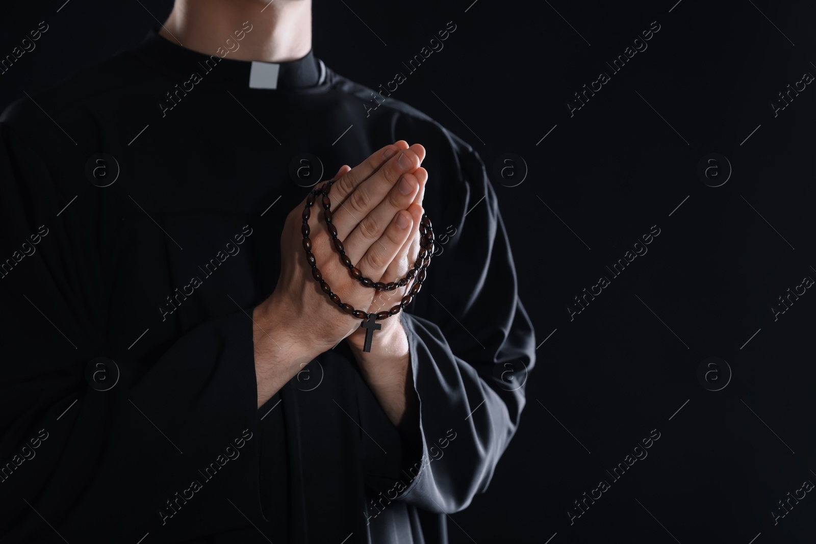 Photo of Priest with rosary praying on black background, closeup. Space for text