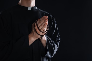 Photo of Priest with rosary praying on black background, closeup. Space for text