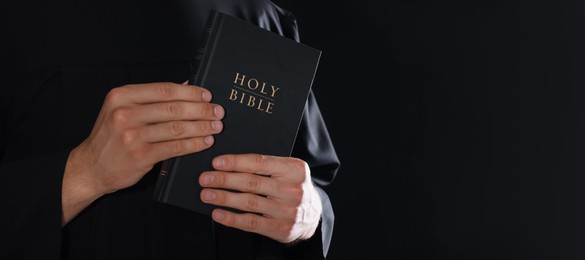 Photo of Priest with Holy Bible on black background, closeup. Space for text