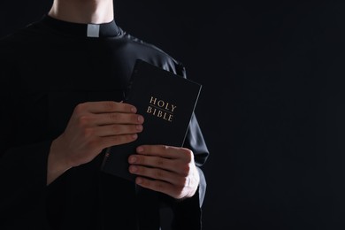 Photo of Priest with Holy Bible on black background, closeup. Space for text