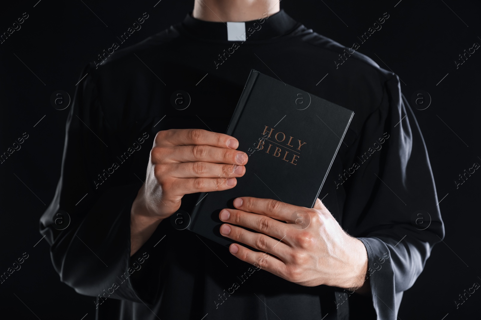 Photo of Priest with Holy Bible on black background, closeup