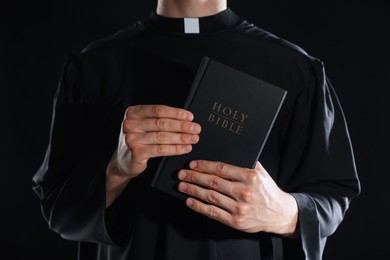 Photo of Priest with Holy Bible on black background, closeup