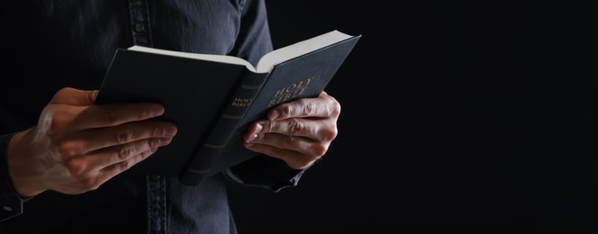 Photo of Priest with Holy Bible on black background, closeup. Space for text