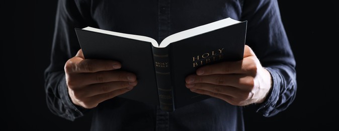 Photo of Priest with Holy Bible on black background, closeup